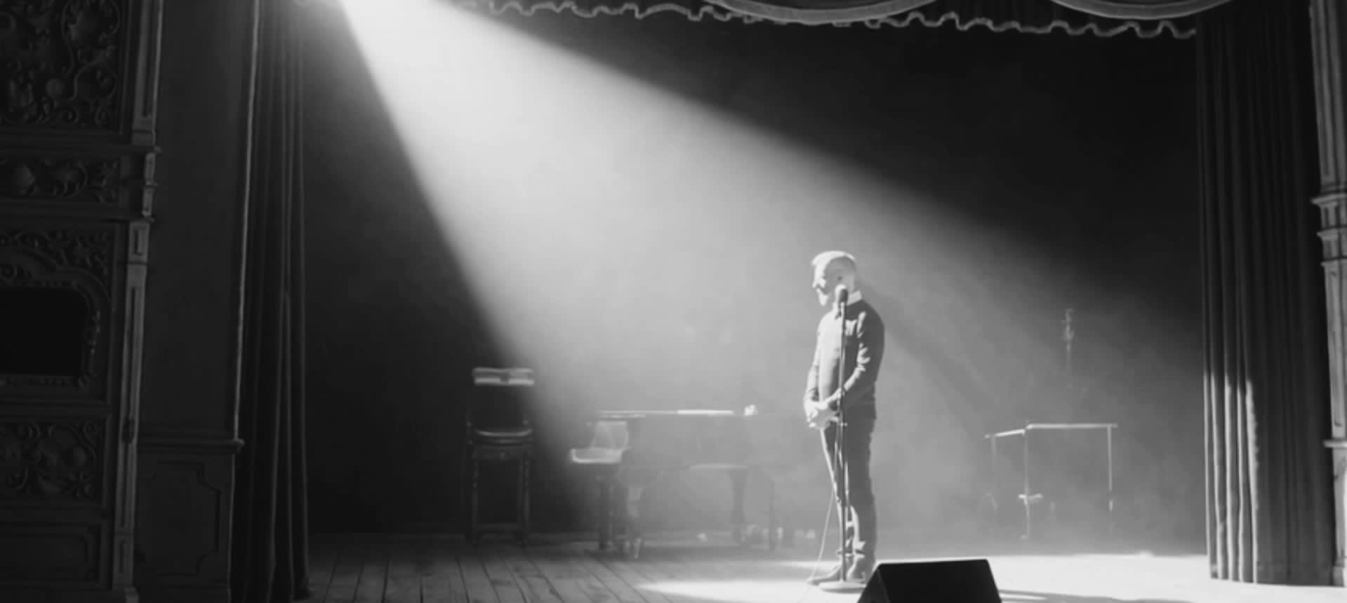EgoB standing on a wide stage under a spotlight